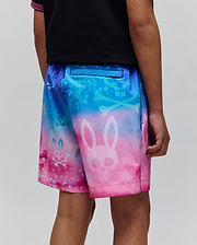 Kids Caspian Swim Trunk in a vibrant blue to pink gradient, featuring an all-over print of large and small Psycho Bunny skull and crossbones logos with a splatter effect.