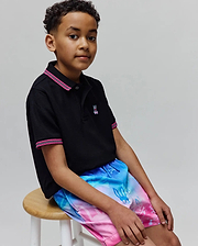 Black pique polo with pink/white striped collar and cuffs, featuring a small embroidered Psycho Bunny logo, paired with Kids Caspian Swim Trunk in a blue-to-pink gradient with allover bunny skull pattern.