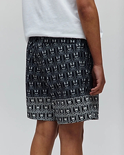 Kids Keon Swim Trunk, black with white all-over Psycho Bunny skull logo pattern, classic fit, smooth quick-dry fabric, and a distinctive bordered hem.