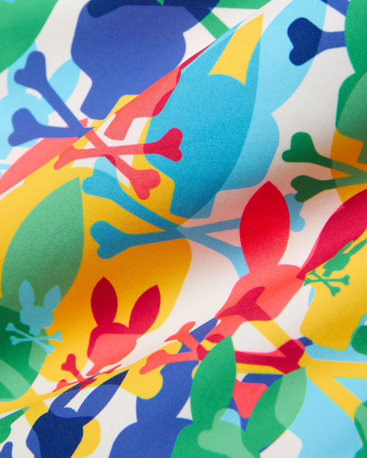 Kids Tanner Swim Trunk featuring a vibrant all-over print of overlapping Psycho Bunny skull and crossbones logos in red, blue, yellow, and green on a smooth white fabric.