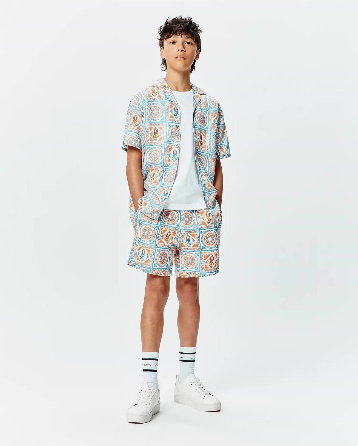 Kids Frank Swim Trunk and matching short-sleeve shirt, relaxed fit, with a vibrant light blue and orange geometric tile pattern featuring integrated small Psycho Bunny skull logos.