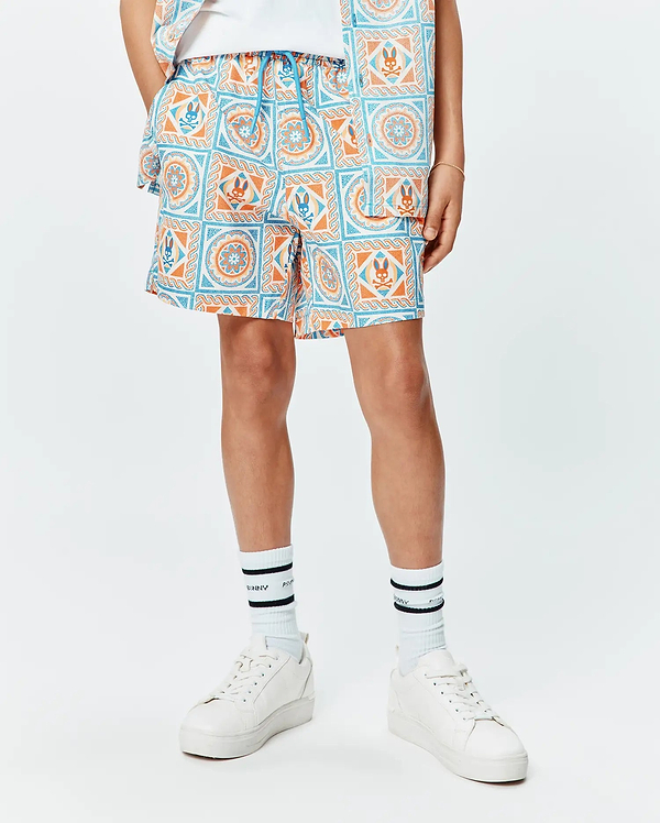 Kids Frank Swim Trunk, a relaxed fit swim trunk featuring a vibrant white, blue, and orange tiled pattern with repeated Psycho Bunny skull logos and a blue drawstring.