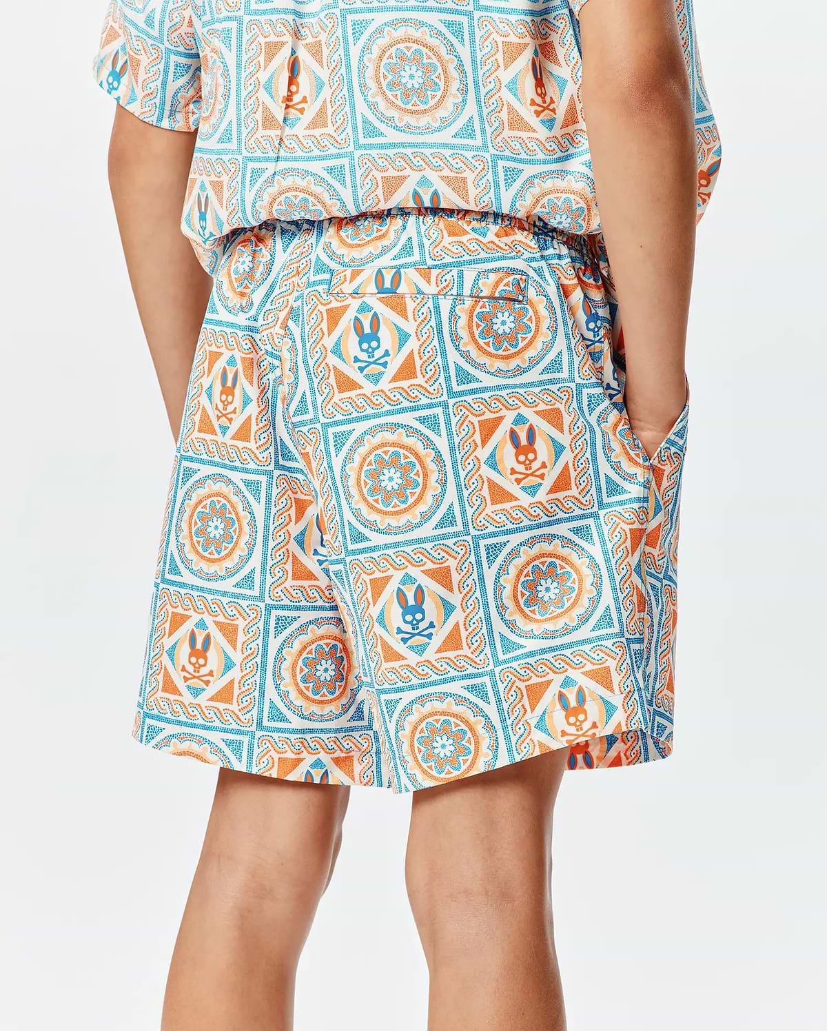 Kids Frank Swim Trunk in a relaxed fit, featuring a vibrant white, orange, and blue mosaic tile pattern with integrated Psycho Bunny skull logos, elastic waistband, and side pockets.