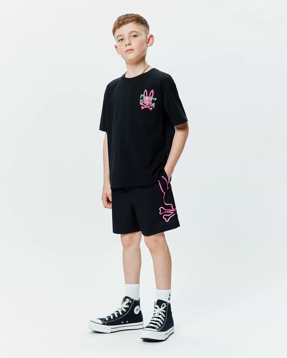 Black relaxed fit jersey t-shirt with a pink and green Psycho Bunny skull logo on the chest, paired with black Kids Duncan Bunny Print Swim Trunk featuring a large pink outline bunny skull logo on the left leg.