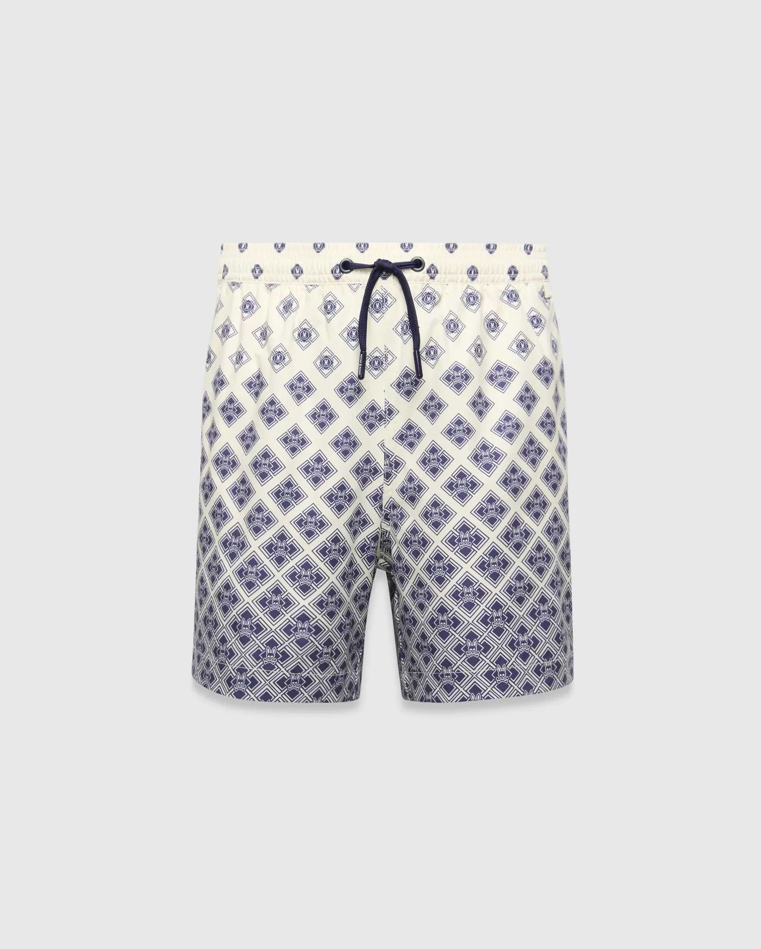 Kids Tobias Swim Trunk in cream with a navy blue diamond grid pattern featuring repeated Psycho Bunny skull logos, a relaxed fit, and a navy drawstring. The pattern intensifies towards the hem.