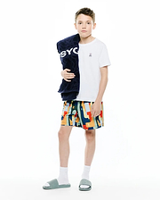 White jersey t-shirt with small embroidered Psycho Bunny logo, paired with Kids Wes All Over Print Swim Trunk featuring a vibrant geometric pattern and logo, plus a navy terry towel with large PSYCHO text. (4)