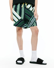 Kids Drew All Over Print Swim Trunk, a relaxed fit short with a dynamic patchwork of green, navy, white, and yellow stripes, featuring a bright yellow drawstring.