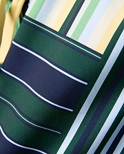 Kids Drew All Over Print Swim Trunk featuring a vibrant geometric pattern of dark green, navy, light blue, light green, white, and yellow stripes on smooth woven fabric.
