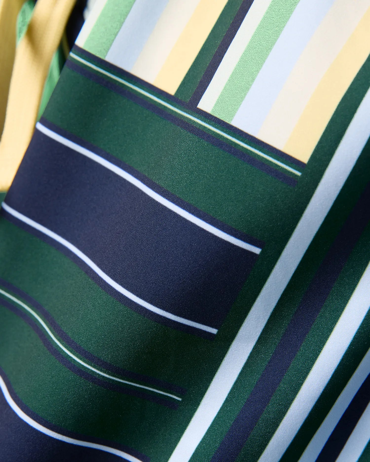 Kids Drew All Over Print Swim Trunk featuring a vibrant geometric pattern of dark green, navy, light blue, light green, white, and yellow stripes on smooth woven fabric.