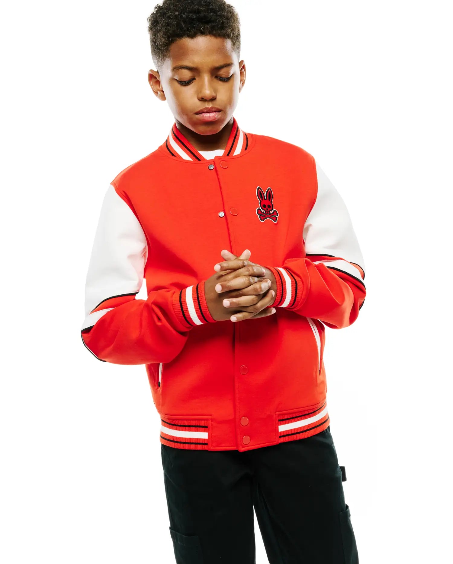 Kids Joey Knit Bomber, a red varsity jacket with white contrast sleeves, classic fit, ribbed collar, cuffs, and hem with black and white stripes, and an embroidered Psycho Bunny skull logo on the left chest.