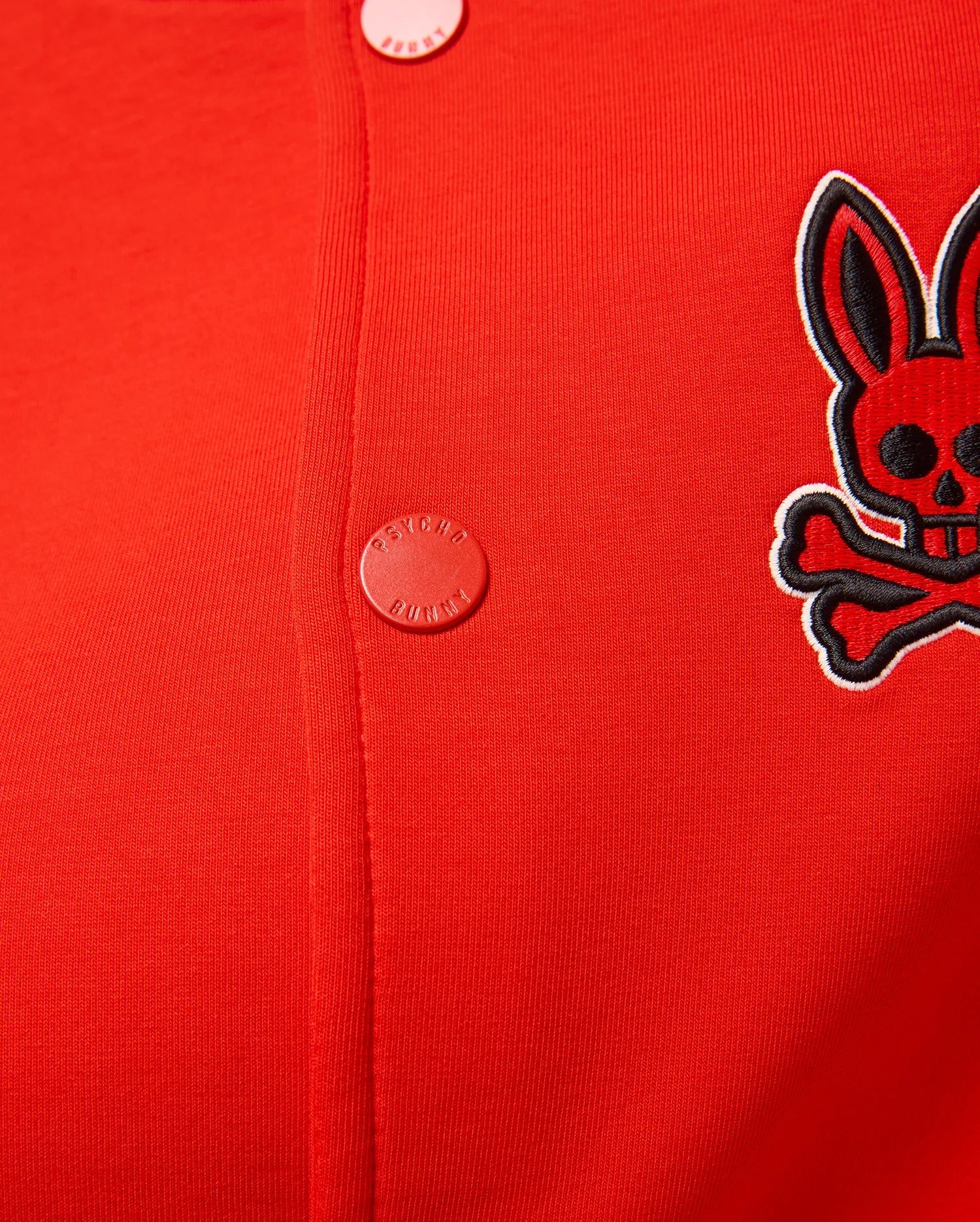 Kids Joey Knit Bomber in vibrant red, featuring a fine ribbed knit texture, an embroidered black and white Psycho Bunny skull logo on the left chest, and red branded snap buttons.