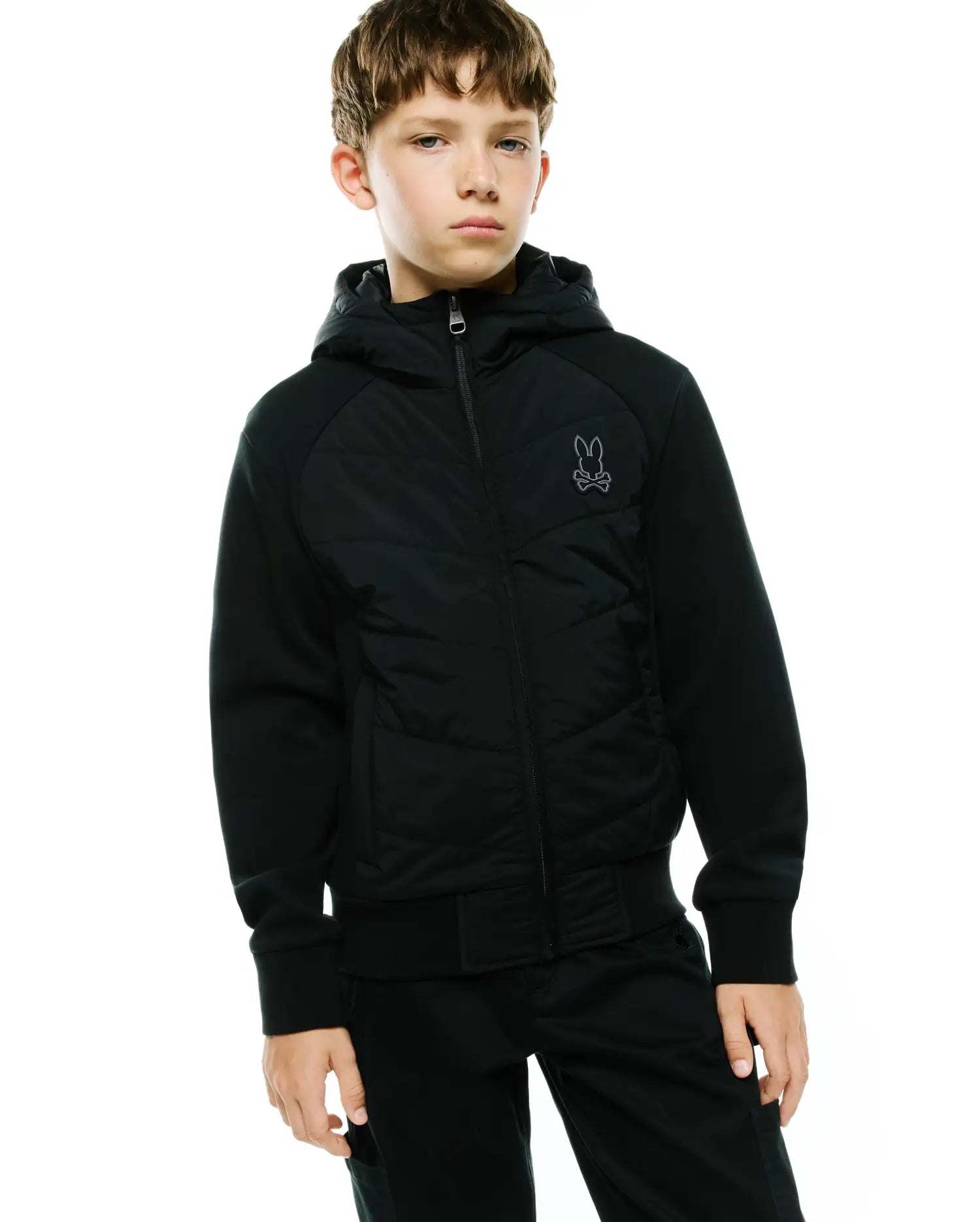 Kids Gordley Mix Media Jacket, black, classic fit, hooded full-zip with quilted front panel, jersey sleeves, ribbed cuffs/hem, and a small embroidered dark grey Psycho Bunny skull logo on the left chest.