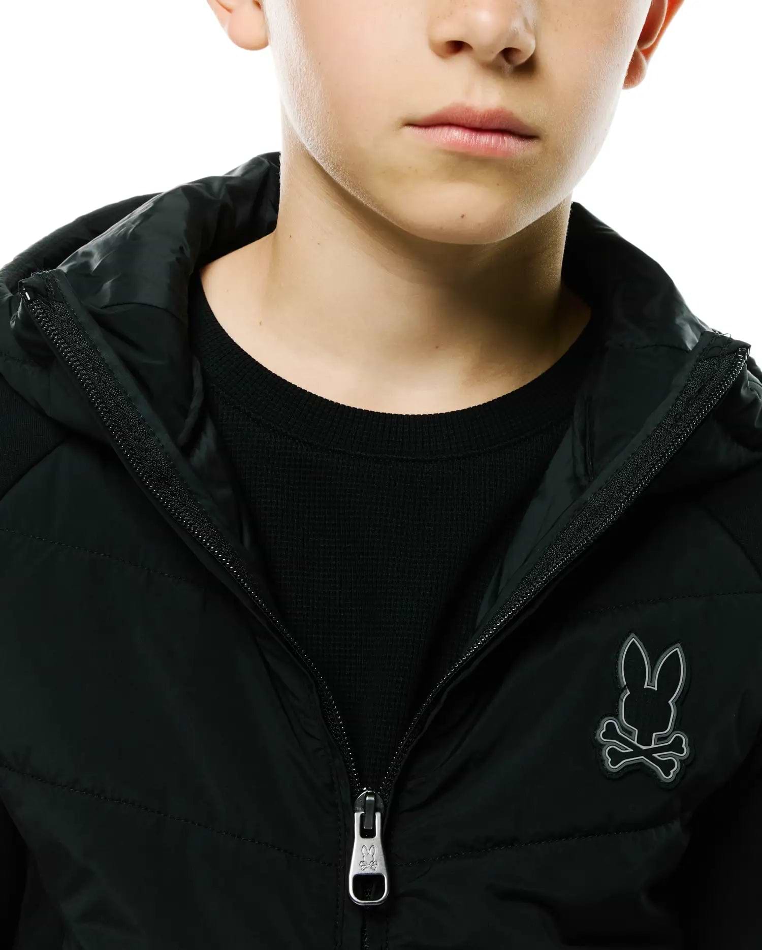 Kids Gordley Mix Media Jacket in black, featuring a padded front, waffle knit sleeves, full zip closure with a Psycho Bunny logo pull, and a prominent grey embroidered bunny skull logo on the left chest.