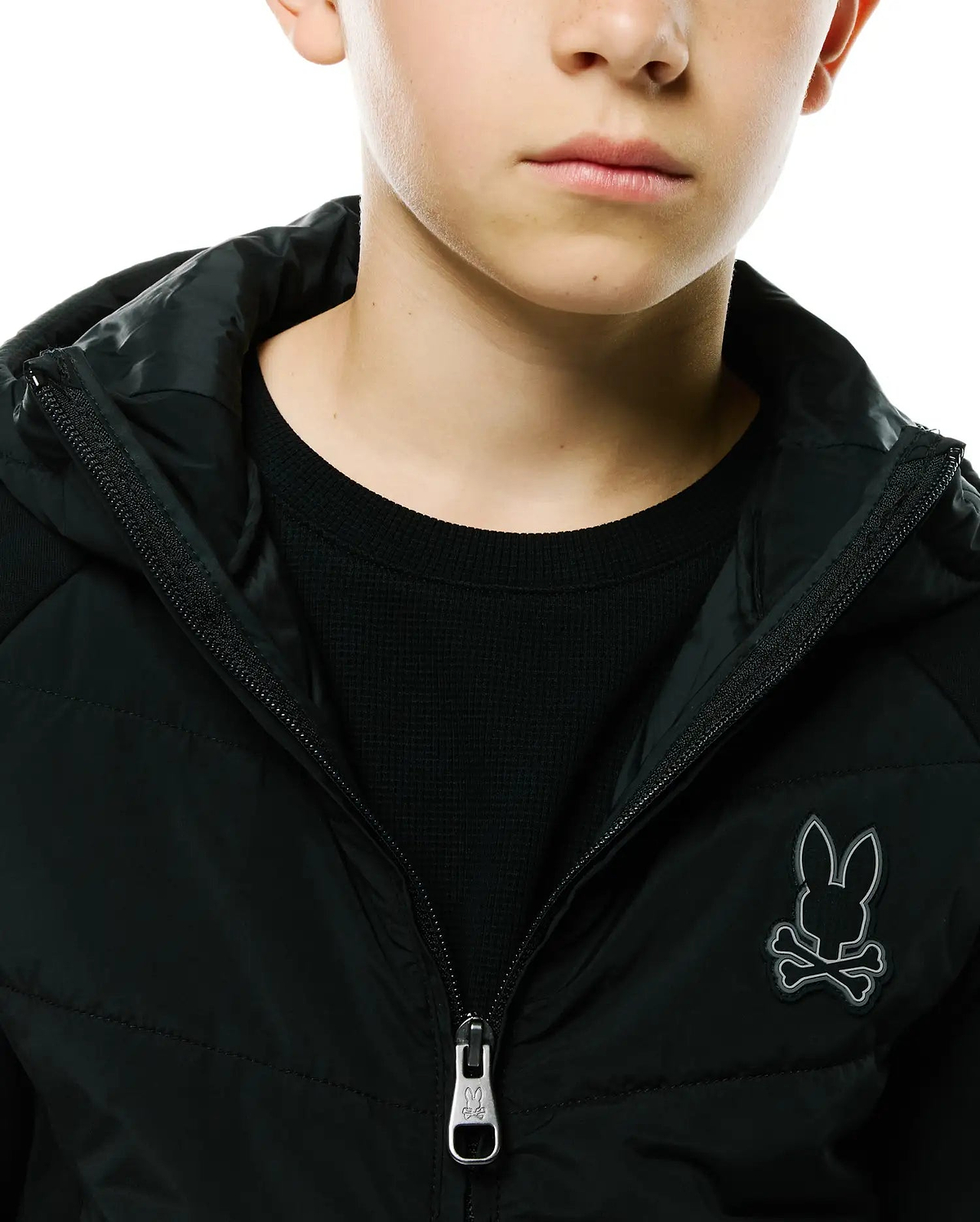 Kids Gordley Mix Media Jacket in black, featuring a padded front, waffle knit sleeves, full zip closure with a Psycho Bunny logo pull, and a prominent grey embroidered bunny skull logo on the left chest.