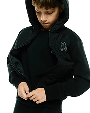 Kids Gordley Mix Media Jacket, a black hooded full-zip jacket with a quilted front panel, soft jersey sleeves, and an embroidered grey Psycho Bunny skull logo on the left chest.