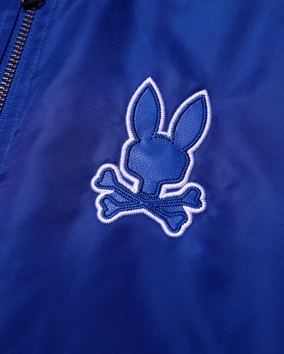 Kids Nathaniel Satin Coach Jacket in smooth royal blue, featuring a prominent textured dark blue Psycho Bunny skull logo with a thick white embroidered outline. (6)