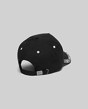 Black Kids Luke Trucker Cap featuring white embroidered eyelets, a white bandana-style pattern on the side brim, and a small engraved Psycho Bunny skull logo on the metal adjustable back clasp.