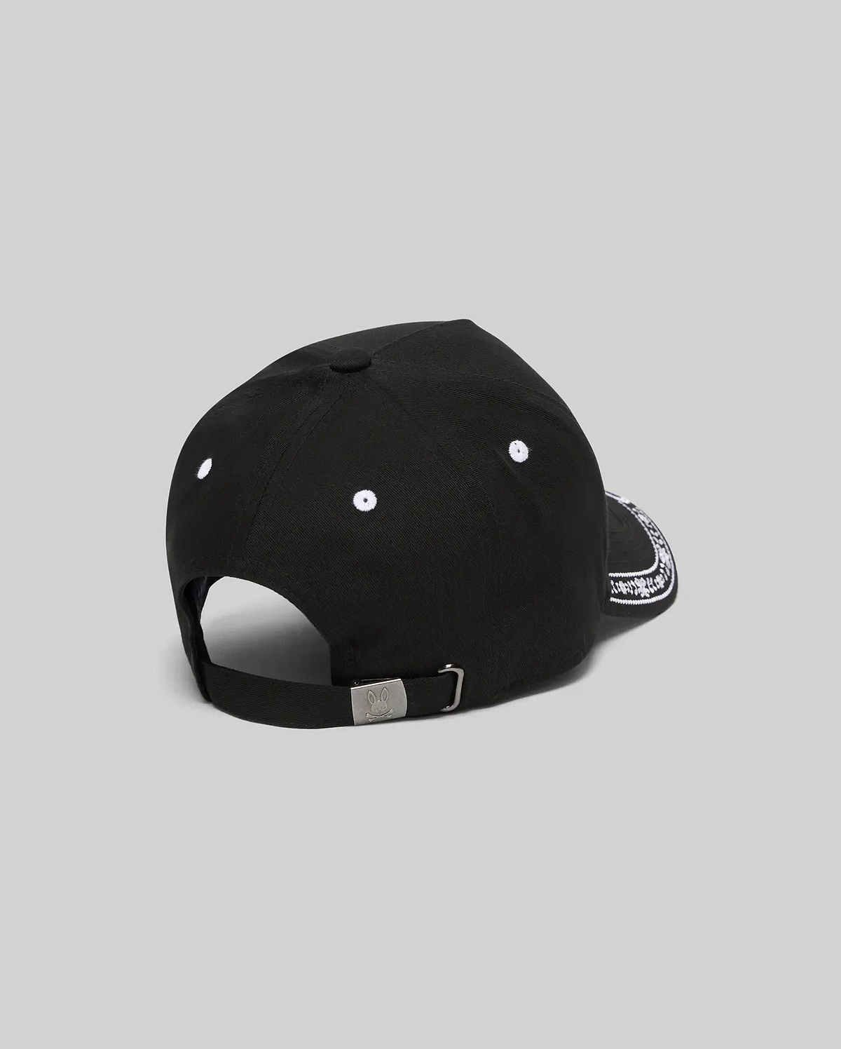 Black Kids Luke Trucker Cap featuring white embroidered eyelets, a white bandana-style pattern on the side brim, and a small engraved Psycho Bunny skull logo on the metal adjustable back clasp.