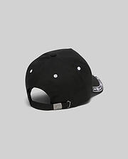 Black Kids Luke Trucker Cap featuring white embroidered eyelets, a white bandana-style pattern on the side brim, and a small engraved Psycho Bunny skull logo on the metal adjustable back clasp.