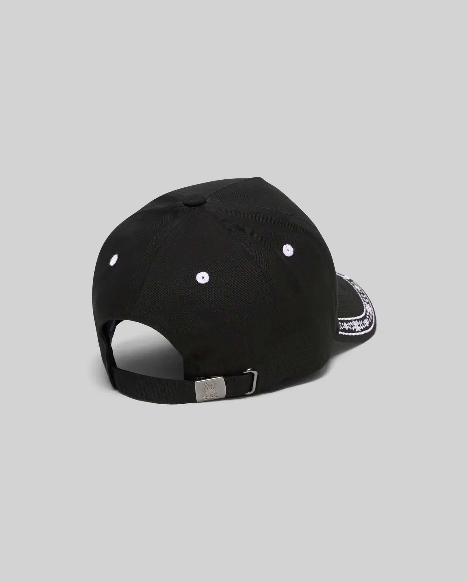 Black Kids Luke Trucker Cap featuring white embroidered eyelets, a white bandana-style pattern on the side brim, and a small engraved Psycho Bunny skull logo on the metal adjustable back clasp.