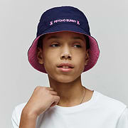 Kids Luke Reversible Bucket Hat in Navy Blue, reversing to Pink, with pink embroidered Psycho Bunny text and skull logos, plus a white jersey t-shirt featuring a small embroidered Psycho Bunny skull logo.