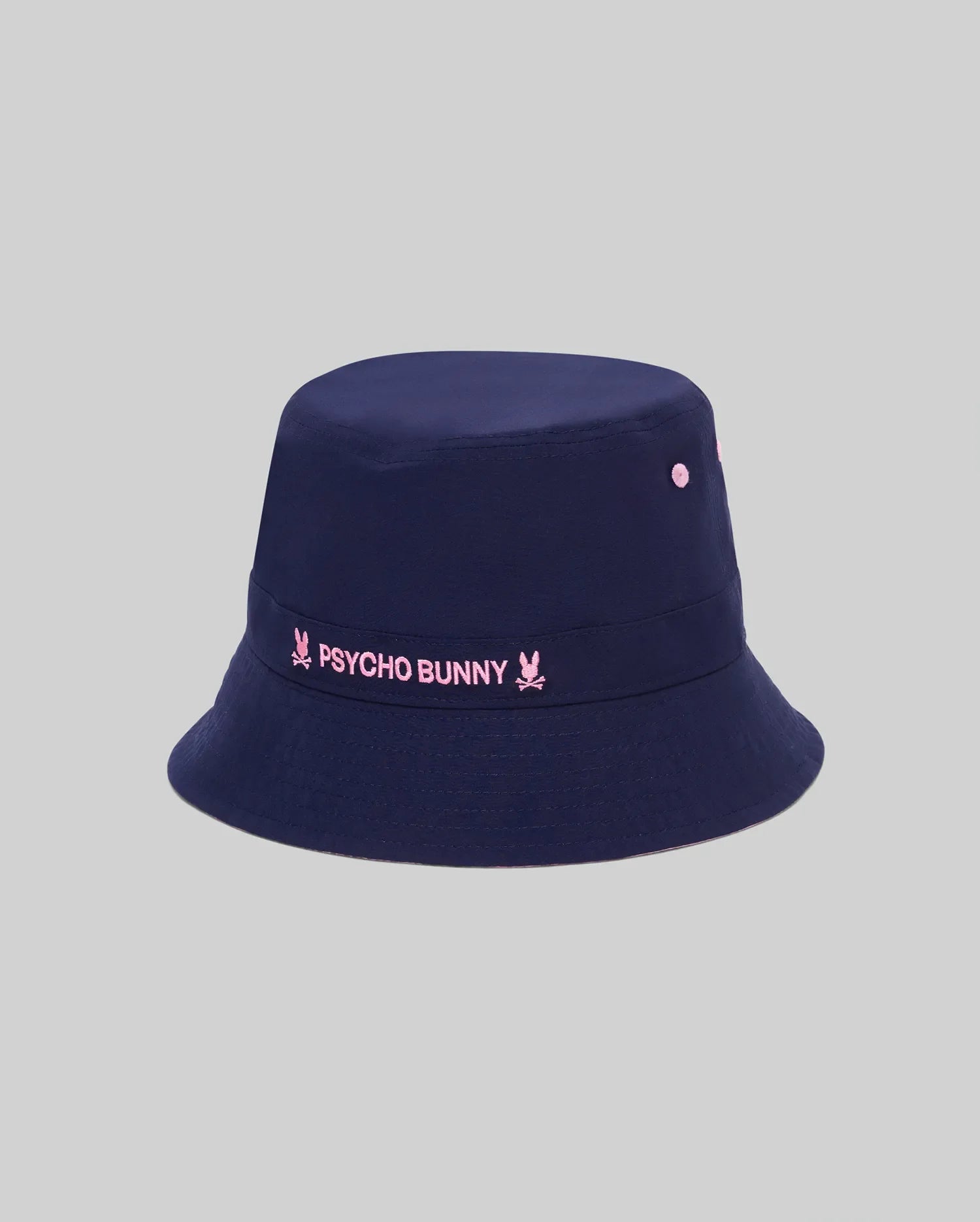 Kids Luke Reversible Bucket Hat in navy, featuring a prominent embroidered pink Psycho Bunny text logo with bunny skull icons on the front band and matching pink ventilation eyelets.