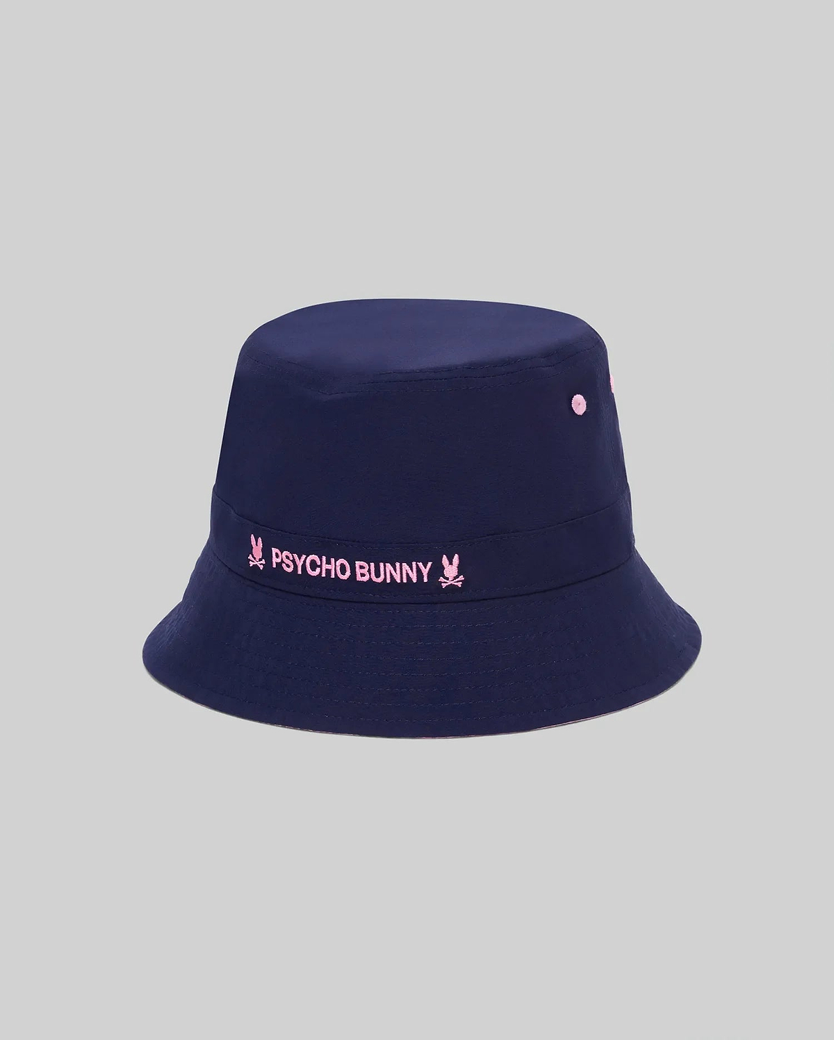 Kids Luke Reversible Bucket Hat in navy, featuring a prominent embroidered pink Psycho Bunny text logo with bunny skull icons on the front band and matching pink ventilation eyelets.