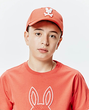 Coral jersey t-shirt with a large, textured coral Psycho Bunny logo outlined in white on the chest, paired with a matching Kids Craig Baseball Cap featuring a white embroidered bunny skull.