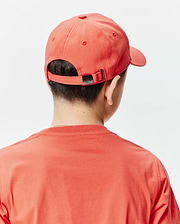 Vibrant coral KIDS CRAIG BASEBALL CAP, featuring a small black Psycho Bunny skull logo on its adjustable metal buckle, complementing a relaxed fit coral jersey t-shirt.