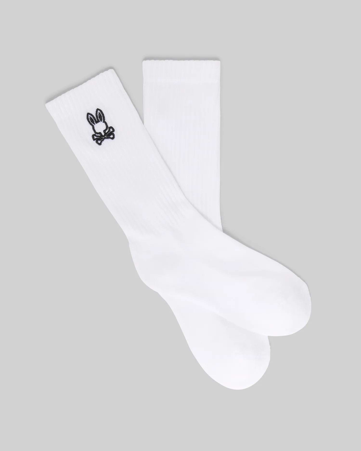 The Psycho Bunny KIDS 3 PACK SPORT SOCK (KO2200001) includes white crew socks made with soft Pima cotton and spandex, each featuring a small black bunny skull and crossbones logo near the top. Displayed on a gray background.