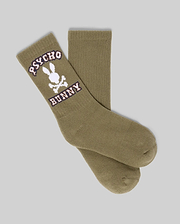 The Psycho Bunny KIDS 3 PACK SPORT SOCKS (KO2200005) includes durable cotton socks in olive green with a white skull and bunny logo plus "PSYCHO BUNNY" in white and purple, displayed on a plain gray background.
