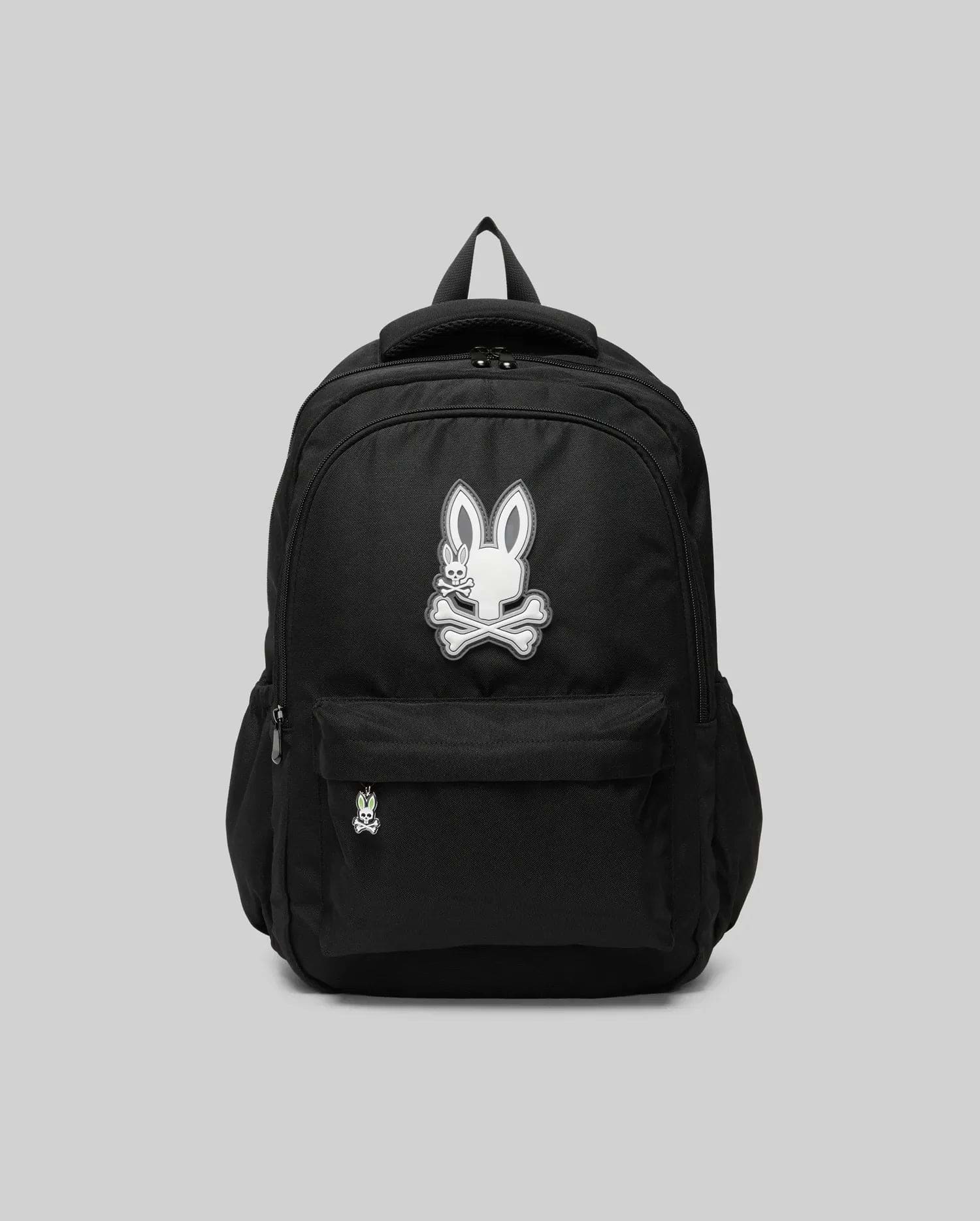The Psycho Bunny KIDS PSYCHO BUNNY BACKPACK - KO2400004 displays a white cartoon bunny and crossbones emblem on the front pocket. Made from durable canvas with padded, adjustable straps, it is shown on a plain gray background.