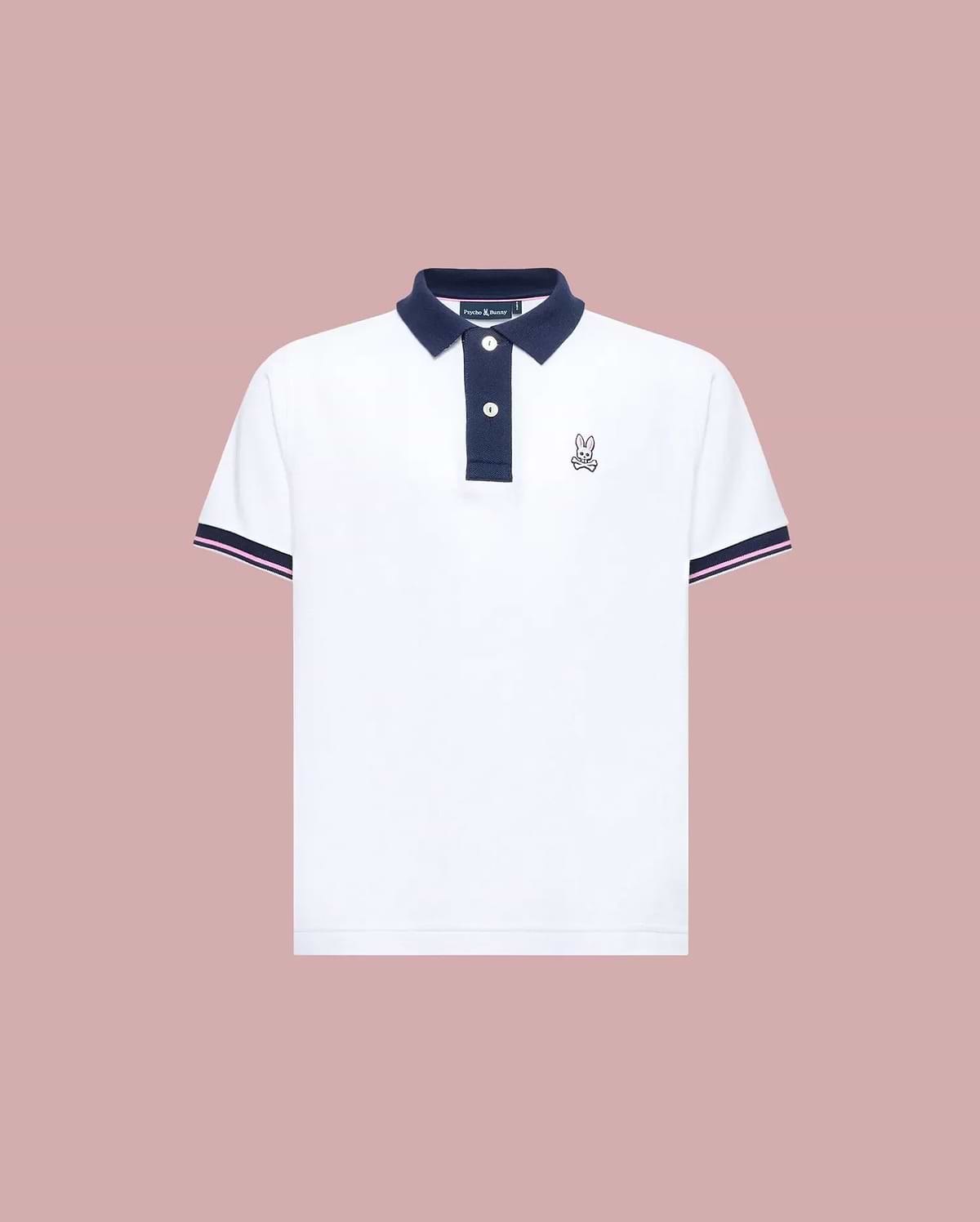 The Psycho Bunny KIDS ARCHIVE CLASSIC BUNNY PIQUE POLO (KT0100010) is a white, short-sleeve Pima cotton shirt with a navy collar and trim, three dark buttons, and an embroidered Bunny logo on the left chest, shown on a pale pink background.