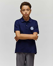 A boy with short curly hair stands against a plain background, arms crossed and neutral-faced, wearing the Psycho Bunny KIDS AUGUSTE PIQUE POLO - KT0100033 in varsity-style navy blue and gray pants. (3)