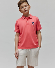 Kids Ara Pique Polo in coral, classic fit, pique fabric. Features a small, multi-color embroidered Psycho Bunny skull logo on the left chest and white tipping on the ribbed collar and cuffs.