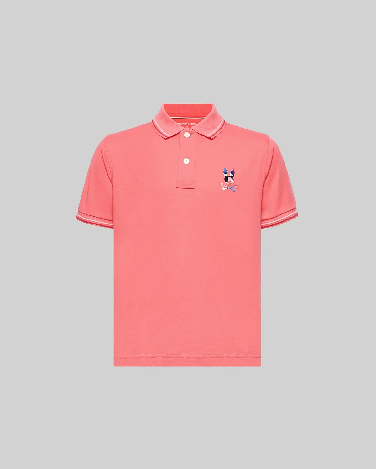 Kids Ara Pique Polo in coral pink, featuring a classic fit, pique knit fabric, white two-button placket, ribbed collar and cuffs with white tipping, and a small embroidered multi-color Psycho Bunny skull logo on the left chest.
