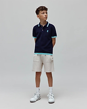 Kids Dax Knit Polo in navy, with light blue and white striped collar, cuffs, and hem. Features a small embroidered light blue Psycho Bunny skull logo on the chest. Paired with light beige knit shorts.