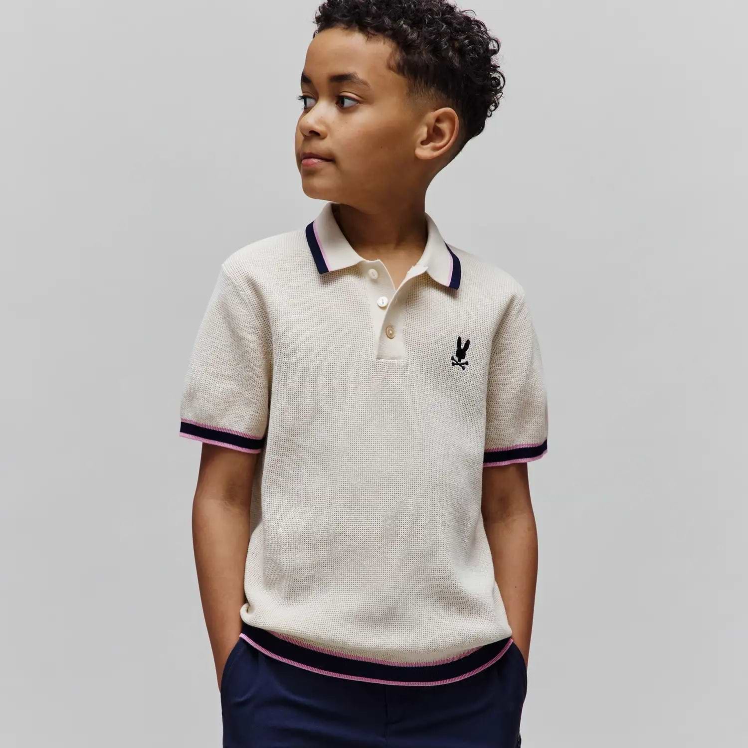 Kids Dax Knit Polo, cream waffle knit with navy and pink striped tipping on collar, cuffs, and hem, featuring a small embroidered black Psycho Bunny skull logo on the left chest.