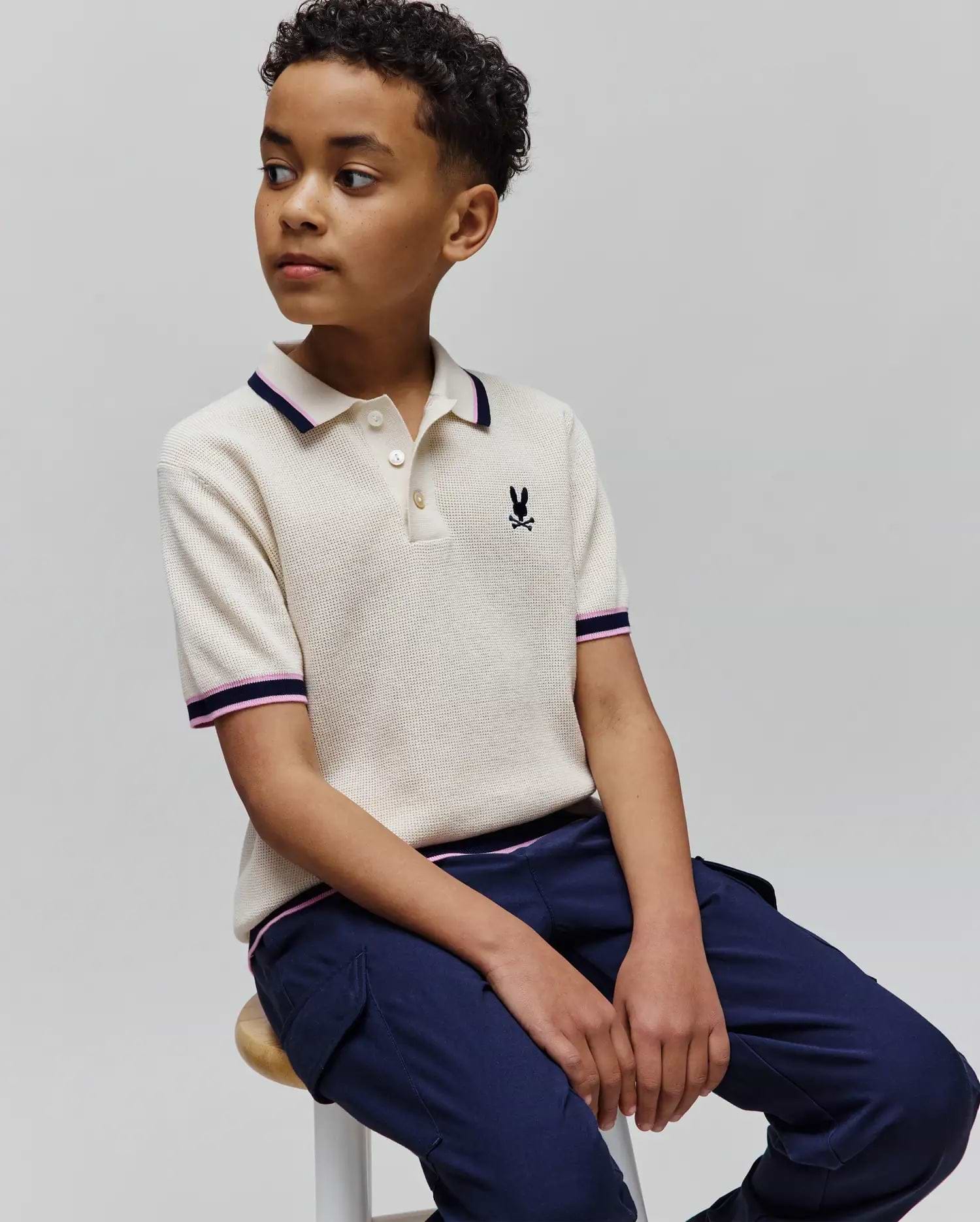Kids Dax Knit Polo in cream waffle knit with navy and pink striped collar and cuffs, featuring a small embroidered Psycho Bunny skull logo on the left chest.