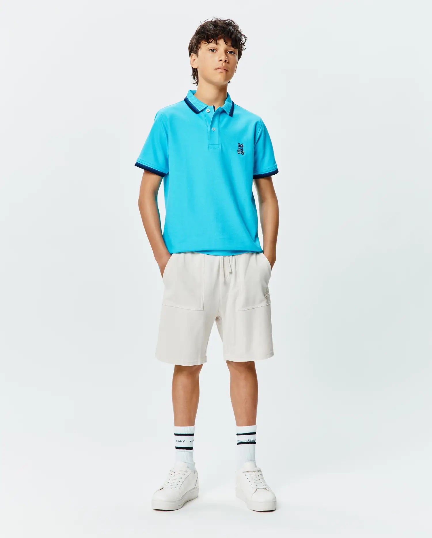 Kids Holden Pique Polo in bright blue, classic fit, featuring a navy blue collar with a subtle dot pattern and matching cuffs, plus a small embroidered Psycho Bunny skull logo on the left chest. (4)