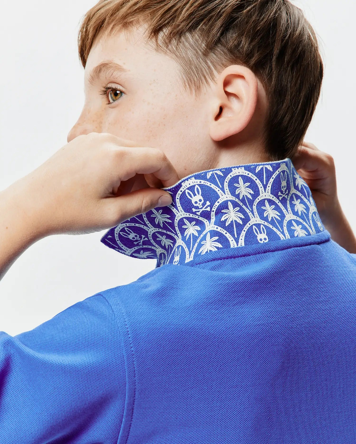 Kids Brad Pique Polo in vibrant royal blue, featuring a classic pique texture and a distinctive inner collar with a white repeating pattern of Psycho Bunny skull logos and palm trees.