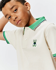 Kids Sunny Pique Polo in cream, featuring a classic fit, green ribbed collar with navy stripe, matching striped cuffs, and a small embroidered green Psycho Bunny skull with blue sunglasses on the left chest. (1)