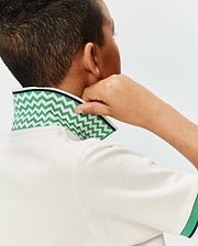 Kids Sunny Pique Polo in cream pique fabric, featuring a bold green and white chevron pattern on the collar with a navy trim, and matching green and navy striped cuffs. (2)