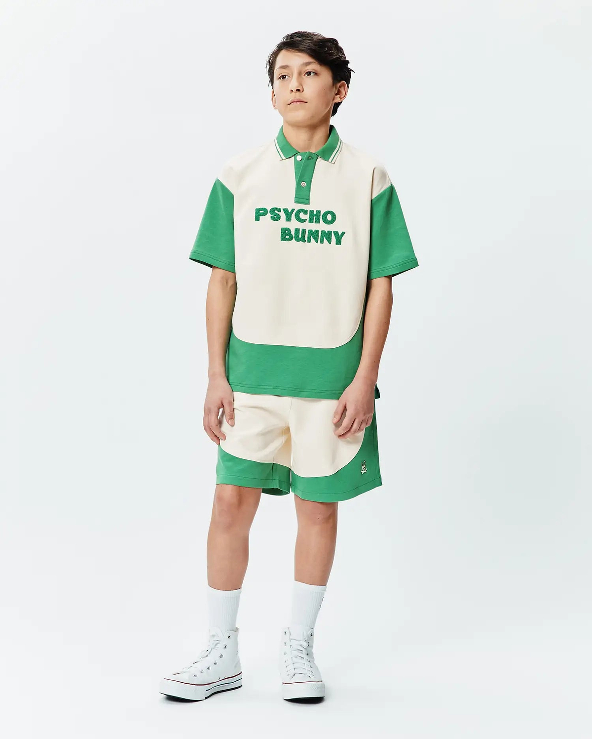 Kids Kelly Oversized Polo, a cream and green color block jersey polo with large PSYCHO BUNNY chest text. Matching relaxed fit shorts feature a small side bunny skull logo.