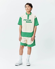 Kids Kelly Oversized Polo, a cream and green color block jersey polo with large PSYCHO BUNNY chest text. Matching relaxed fit shorts feature a small side bunny skull logo.