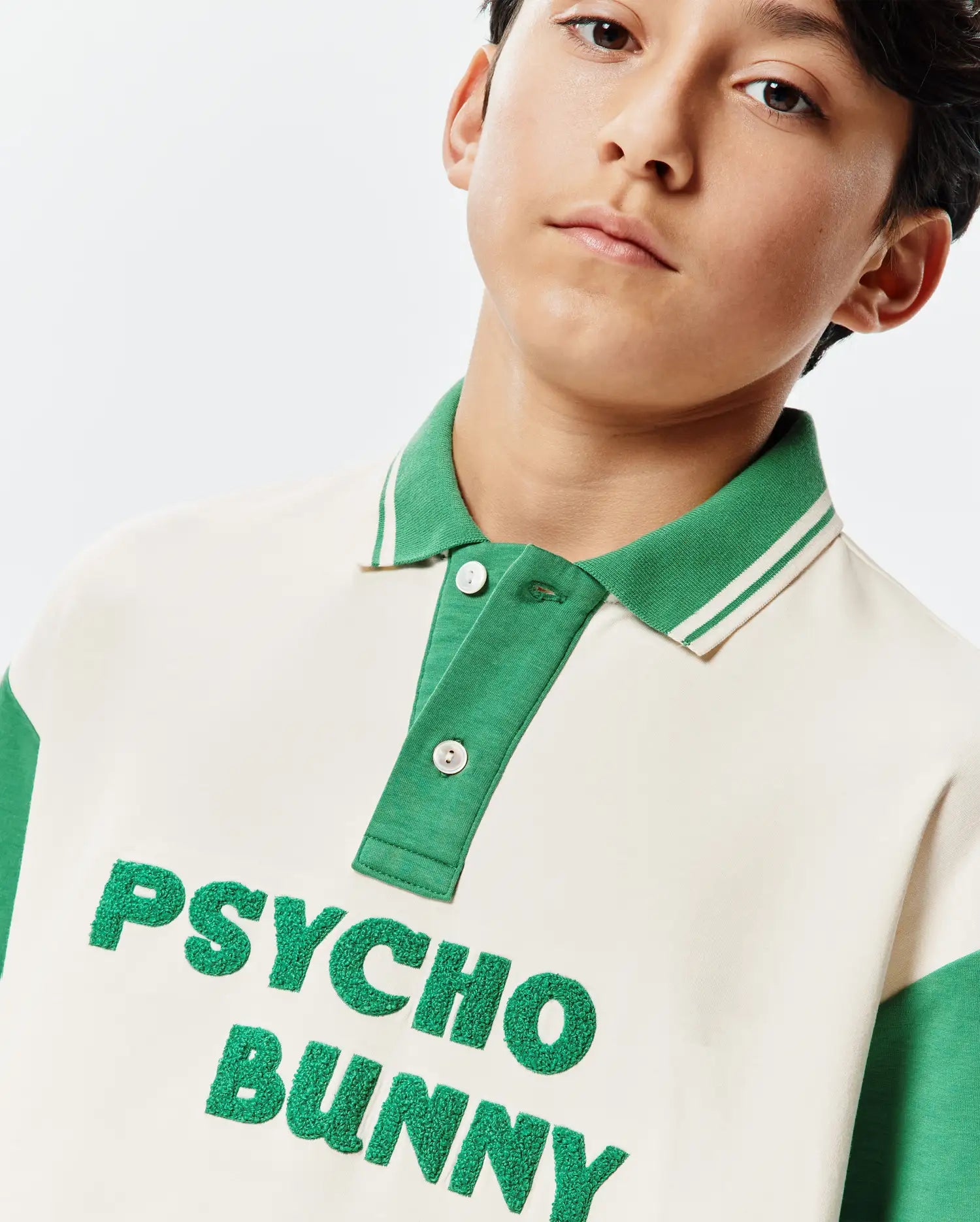 Kids Kelly Oversized Polo, a cream and green color-block jersey polo featuring a ribbed striped collar, two-button placket, and large textured green embroidered Psycho Bunny text on the chest.