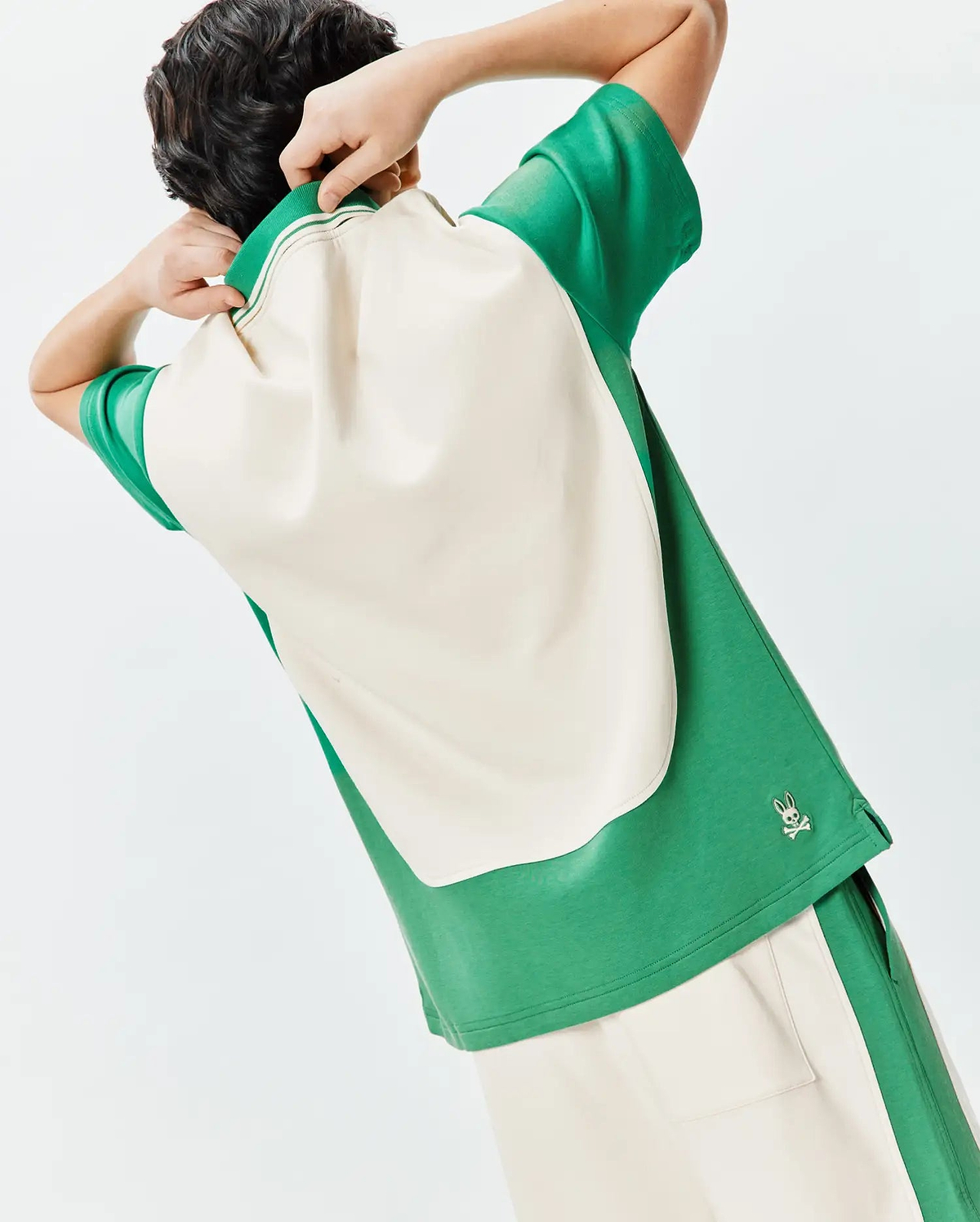 Kids Kelly Oversized Polo in green and cream color-block jersey, featuring a striped collar, oversized fit, and a small silver embroidered Psycho Bunny skull logo on the lower right hem.
