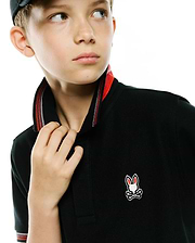 Kids Jaydon Pique Polo, a classic fit black pique polo shirt featuring a red and white striped collar, and a small embroidered Psycho Bunny skull logo on the left chest.
