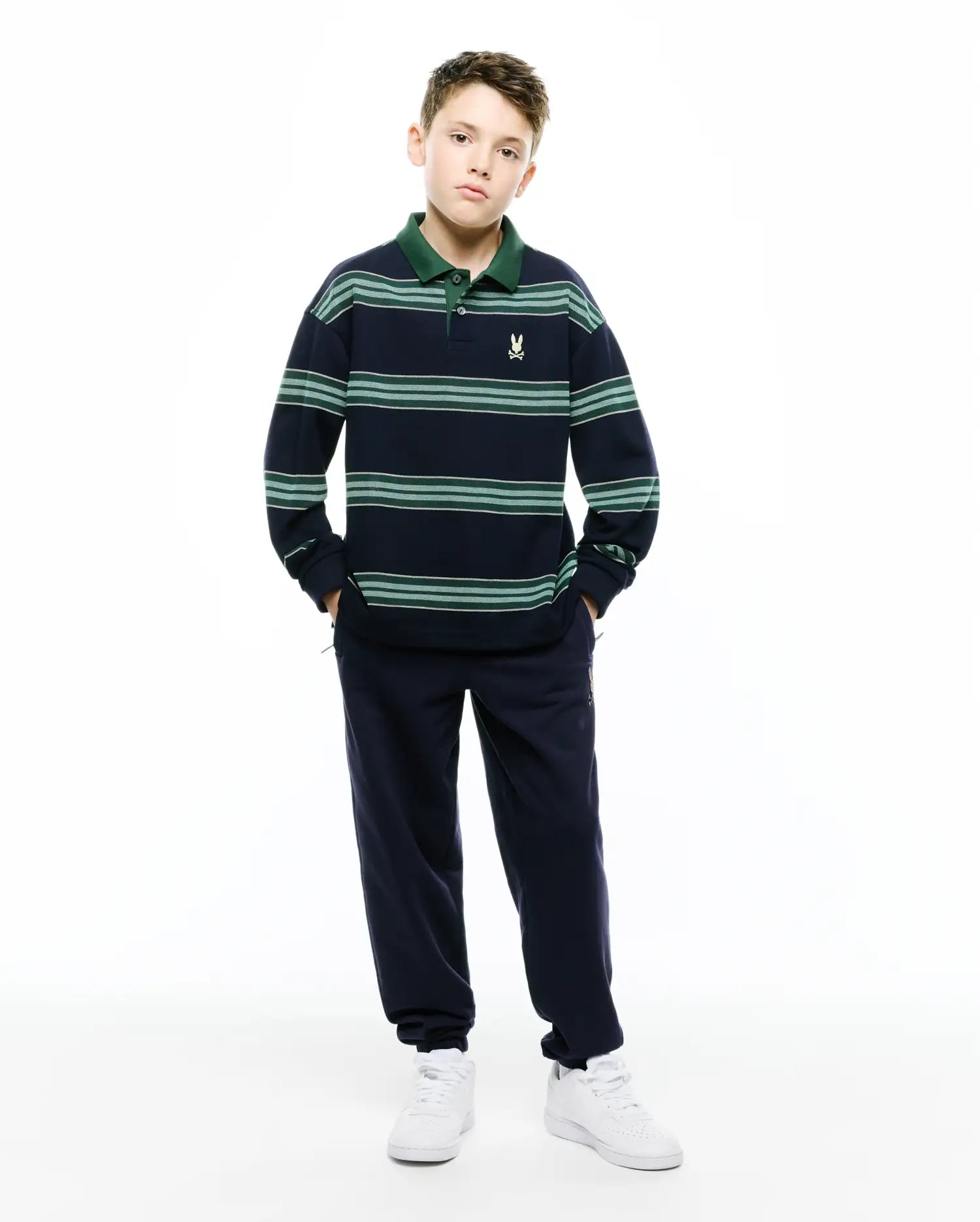 Kids Drew Striped L/S Pique Polo, navy with green stripes and dark green collar, featuring a small embroidered Psycho Bunny skull on chest, paired with navy relaxed sweatpants with subtle thigh logo.