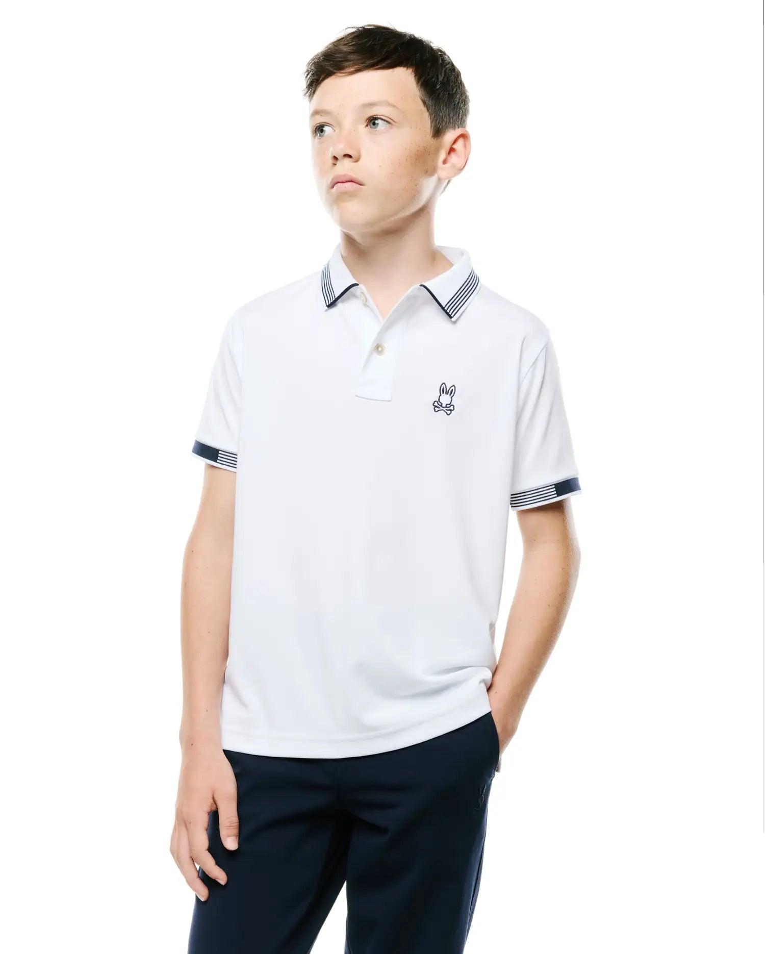 Kids Timmy Pique Polo, white classic fit pique polo with navy blue striped collar and cuffs, featuring a small embroidered Psycho Bunny skull logo on the left chest.
